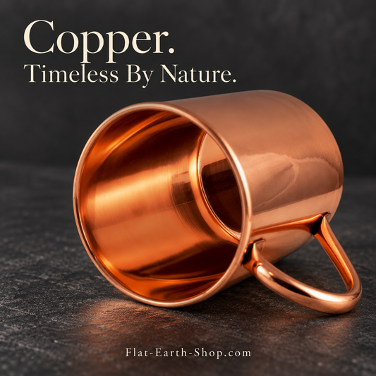 Smooth copper-colored mug lying on its side, showing its open interior and curved handle on a dark stone surface.