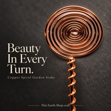 Close-up of the circular spiral top and wire-wrapped stem of a copper-colored garden stake against dark stone.