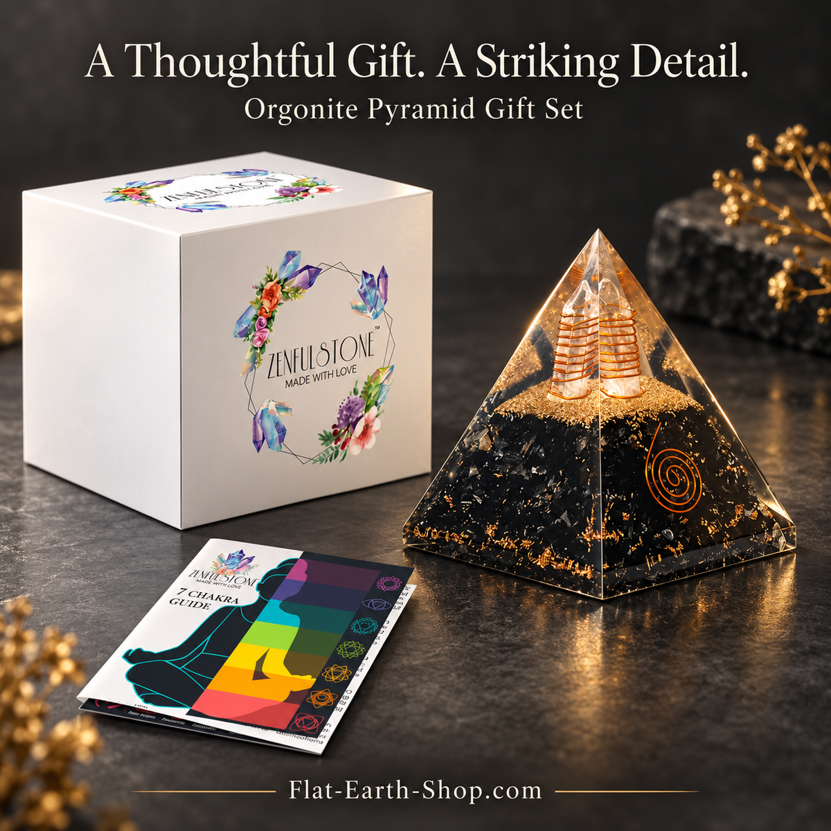 Clear pyramid with black and gold-colored contents, beside a floral white gift box and colorful chakra guide booklet.